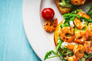 Toast with shrimp, arugula and avocado on a white plate with cherry tomatoes on a blue table. Space for text. Healthy and tasty breakfast concept. Top view. Flat lay.