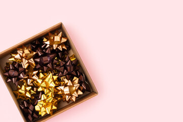 Box with bows made from golden ribbons on a pink background. Preparation for the holidays.