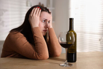Alcohol addiction. Miserable woman with wine at table indoors, selective focus
