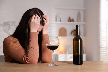 Alcohol addiction. Miserable woman with wine at table indoors