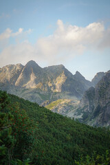 Fototapeta premium Mountain tops with cliffs on blue sky background with few clouds and forest hill slope in the foreground, High Tatra mountains, Slovakia