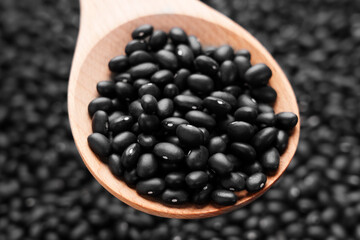 Black turtle beans in a wooden spoon. Dried legume ingredient. Uncooked plant-based food.