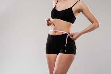 Close-up of a woman measuring her waist with a tape, highlighting fitness, healthy lifestyle, and...