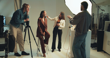 Directing, photography and talking with people in studio together for photoshoot planning. Behind the scenes, creative or media with happy model, makeup artist and photographer getting ready on set