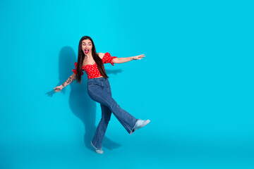 Happy young woman in a casual red top and jeans posing against a vivid blue background expressing joy and creativity
