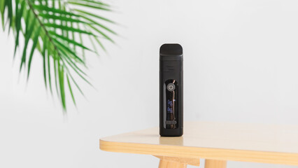 Black dry herb vaporizer on wooden table with palm leaf