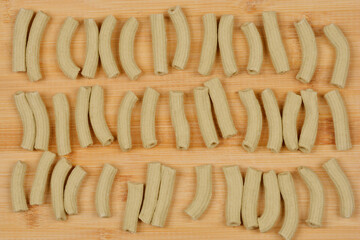 A top-down view of arranged homemade spinach pasta tubes in a rectangular pattern on a wooden surface