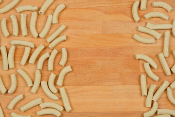A top-down view of scattered homemade spinach pasta tubes on a wooden surface, arranged to leave a rectangular empty space in the center