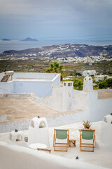 Vertical view of apartment terrace with sage green chairs and aloe plants in Pyrgos Kallistis, the island of Santorini, Greece, with panoramic vista of the Aegean Sea and islands and Greek isle coast