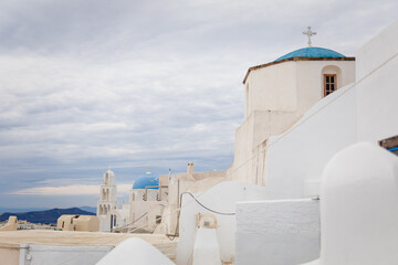 Horizontal view of white Greek orthodox church dome and tower and bells with cross in Pyrgos Kallistis, Santorini, Greece, with cloudy blue sky. A perfect day trip destination from Fira