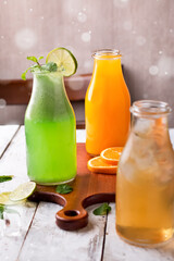 Assorted Drinks including Lemon Mint Drink, Apple Drink, and Orange Juice served in glass bottles on a wooden board side view of Refreshing and vibrant drinks