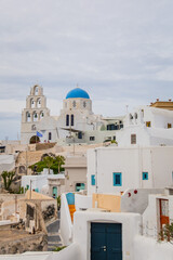 Pyrgos Kallistis, central hilltop village in Santorini, Greece. Vertical view of Saint George Church in historic Greek town with cloudy sky, whitewashed homes, blue domes and traditional architecture