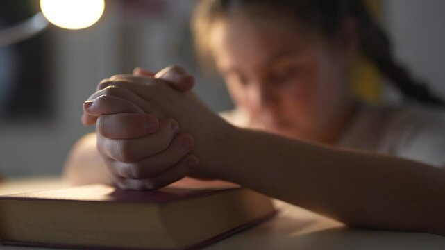 Young girl is praying. Girl lifestyle praying to child in the religion. A book of prayers on a table in the evening. A little girl is saying a prayer.