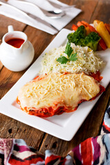 Chicken Parmigiana topped with cheese, Marinara Sauce served on a white plate with rice and vegetables side view Italian cuisine.