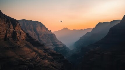 Fototapeta premium Sunset behind rugged mountain peaks, soft orange and pink light illuminating rocky cliffs and valleys