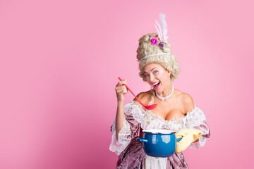 Charming woman in historical baroque costume cooking with vivid expression on a pink background