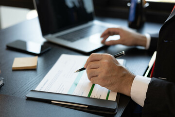 A man in a suit is looking at a piece of paper with graphs on it. He is holding a pen and he is analyzing the data. The scene suggests a professional setting
