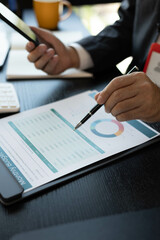 A man in a suit is looking at a piece of paper with graphs on it. He is holding a pen and he is analyzing the data. The scene suggests a professional setting

