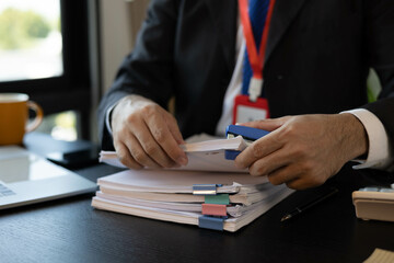 Fototapeta premium A man in a suit is holding a stack of papers and a pen. He is likely working on a project or preparing for a meeting. Concept of professionalism and focus, as the man is fully engaged in his task