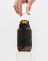 Woman's hand holding amber supplement bottle with capsule in hand