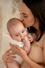 a mother holds a newborn baby in her arms, a mother gently hugs and kisses a small child, maternal love and care, a mom and a baby