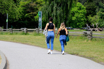 Vue arrière de deux jeunes femmes marchant dans le parc Stanley à Vancouver.