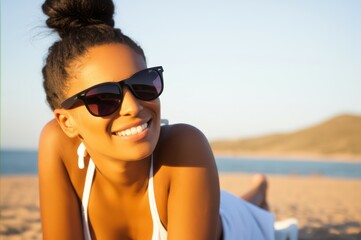 Smiling Black Woman In White Halter Top On Golden Beach Sunny Day By Clear Ocean, With Dark Hair Bun Black Sunglasses, Enjoying Sunny Beach Vibe