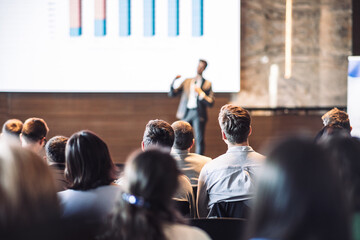 Speaker giving a talk in conference hall at business event. Rear view of unrecognizable people in...