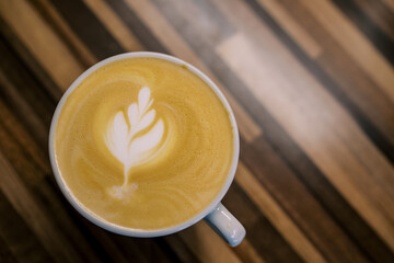 Latte with a leaf on the foam stands in a cup on a wooden table. Top view