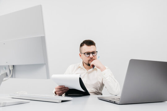 A businessman at a computer in an office, analyzing stock market and inflation charts, sorting through papers. The concept is to capture the tense decision-making process in times of economic instabil