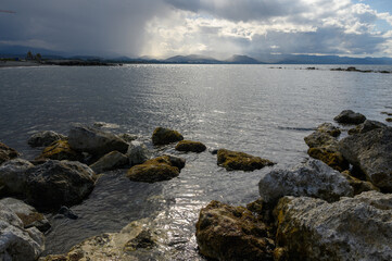Sunlight glimmers on water as waves lap against rocky shore at tranquil seascape