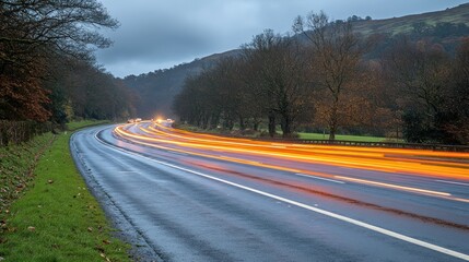 Fototapeta premium Twilight highway curves through autumnal landscape, showcasing light trails from speeding vehicles on a wet road