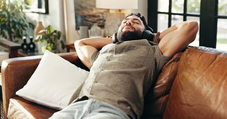 Home, relax and man on couch, headphones and listening to music with weekend break in lounge. Person, headset and guy on sofa, podcast and rest with comfort, radio and audio with song and calm