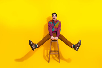 Charming young man in trendy retro-style sweater joyfully posing on a stool against a vibrant yellow background