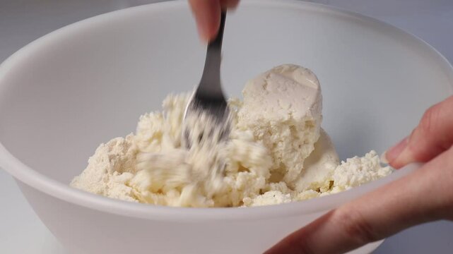 close-up of a woman mixing dough with a fork for cottage cheese pancakes in a white bowl, concept of preparing dough with curd and flour for homemade pancakes.