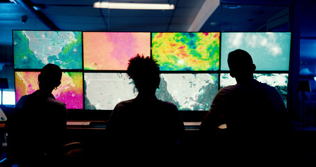 Weather, screen or monitor with people for forecast, satellite maps or teamwork to track storm. Control room, back or scientists with meteorology for broadcast news, report or silhouette at night
