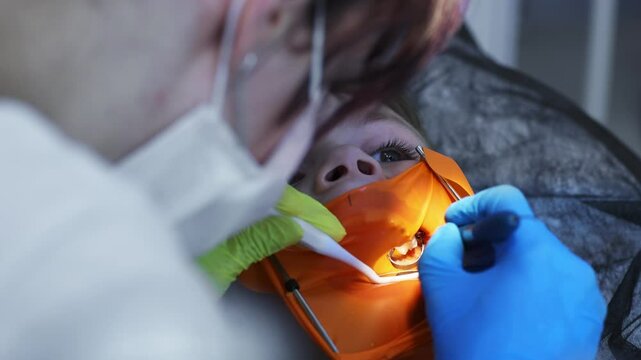 Children's dentistry. First examination at the dentist. A cute handsome boy with his mouth open is looking aside while the doctor is treating her teeth.