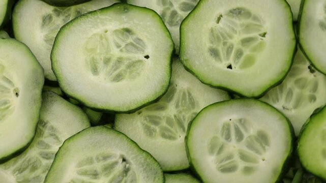 Rotating slides of fresh cucumber in close-up. Green cucumber slices moving in a circular motion. Healthy vegetable background with fresh cucumber slices. top view