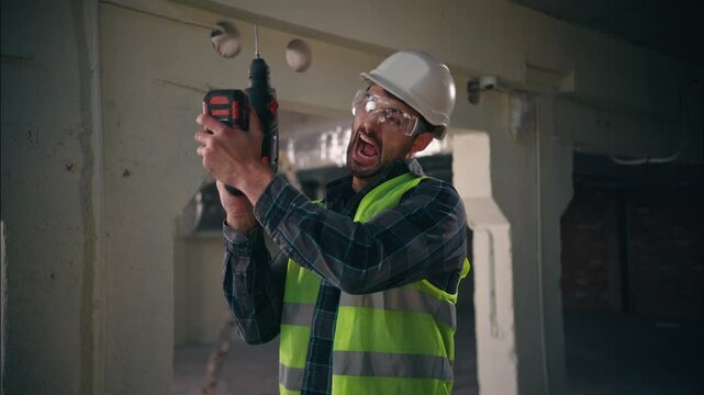 Angry Caucasian foreman male guy engineer man builder holding drill electric tool constructor drilling in factory construction worker doing repairment handyman industrial building repairman screaming