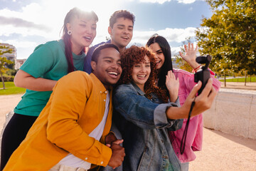 Group of diverse friends taking a selfie in the park, waving at the camera