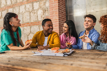 Happy friends eating pizza, laughing and talking together at a restaurant table
