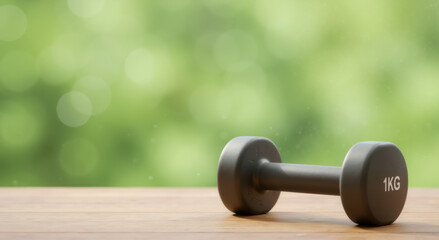 Black dumbbell with 1kg marking on wooden surface against green bokeh background. Fitness equipment concept for home workout programs and strength training advertising