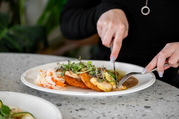 A plate with chicken, hash browns, garnished with fresh microgreens, served with pickles and sauce....