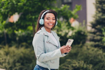 Young woman enjoying music on her headphones while walking outdoors on a sunny day, wearing a...