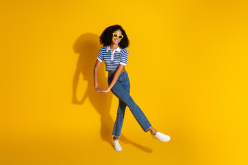 Trendy young woman on a vibrant yellow background wearing striped casual top, stylish sunglasses,...