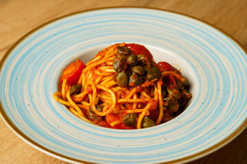 Spaghetti with tomato sauce and capers on a blue-striped plate