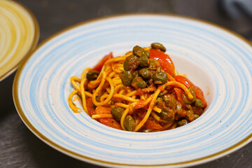 Spaghetti with tomato sauce and capers on a blue-rimmed plate