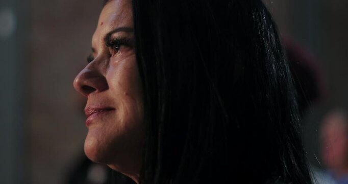 Woman with long dark hair, side profile, listening attentively to a speaker, emotional and reflective with tears in her eyes, part of an engaged audience