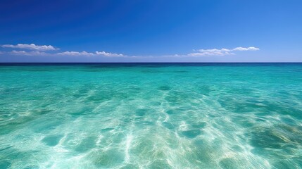 Fototapeta premium Serene turquoise ocean vista under a vibrant blue sky. Crystal clear shallows meet the horizon