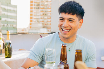 Young Latin man happy on a terrace gathered with friends, celebrating outdoors.